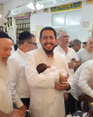 איתמר חמו מחזיק תינוק עטוף ומחייך, המשפחה מסביב