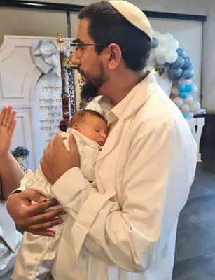 המוהל איתמר חמו מחזיק את התינוק בעדינות לצד כיסא אליהו