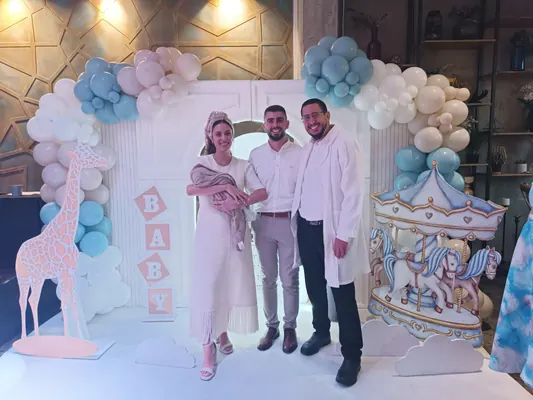 איתמר חמו עם ההורים והתינוק באירוע הברית, קשת בלונים תכלת ולבן